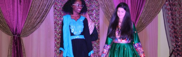 Two girls stand on a purple stage wearing Middle Eastern cultural clothing